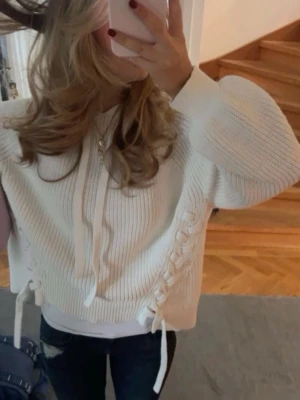 Vit stickad hoodie med snörningar - Säljer en vit stickad hoodie med snörning i sidan och huva med dragsko. Tröjan har ribbade muddar och avslappnad passform, perfekt för en chill och trendig look. Passar till jeans eller leggings. Storlek s lite oversized 💓