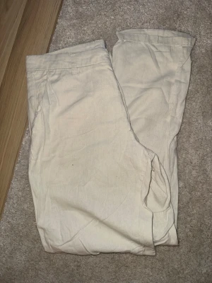Beiga raka linnebyxor - Säljer ett par beiga linnebyxor med rak passform och klassisk midja. Byxorna har enkel design utan synliga detaljer och är tillverkade i ett lätt och luftigt linnematerial. Perfekta för en avslappnad och stilren look.