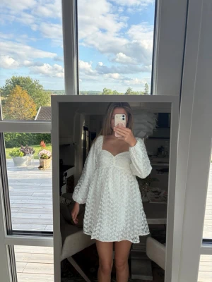 Vit kort klänning med puffärm - Supersöt vit kort klänning med blommigt mönster. Långa puffärmar. Endast använd en gång. Perfekt för skolavslutning/student. (Jag är 176 cm) 