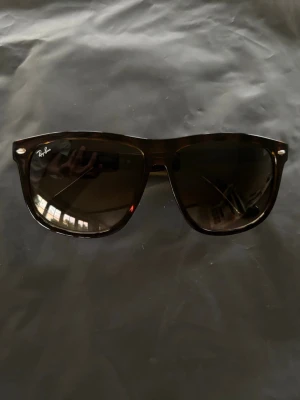 Svarta Ray-Ban solglasögon - Snygga bruna solglasögon från Ray-Ban med klassisk boyfriends. Glasen är mörka och bågarna är i brun plast, vilket ger en stilren och tidlös look. Perfekta för soliga dagar och en cool vibe.