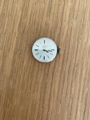 Omega vintage urverk silverfärgat - Säljer ett klassiskt Omega urverk med silverfärgad urtavla och guldfärgade markeringar. Mekaniskt urverk med synliga kugghjul och detaljerad baksida. Perfekt för dig som gillar vintage och vill fixa egen klocka.