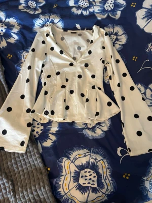 Vit prickig blus från Gina Tricot - Supersnygg vit blus med svarta prickar från Gina Tricot. Blusen har v-ringning, figurnära passform och vida långärmade ärmar. 