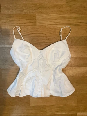 Vit korsettopp från Zapa - Säljer en snygg vit korsettopp från Zara med smala axelband och knappar framtill. Figurnära passform. Perfekt att styla med jeans eller kjol