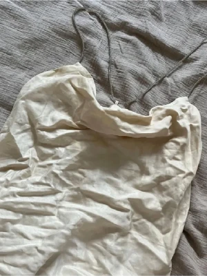Ljusbeige fest topp med smala band - Säljer en ljusbeige linnetopp med tunna, glittriga axelband och enkel, stilren design. Toppen har en mjuk, något lös passform och är perfekt för varma dagar. Materialet känns lätt och svalt mot huden.