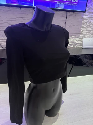 Svart långärmad crop top - Trendig svart långärmad crop top med rund halsringning. Toppen är figurnära och har en enkel, stilren design som passar perfekt till höga jeans eller kjol. Tillverkad i ett mjukt och stretchigt material för en bekväm passform.
