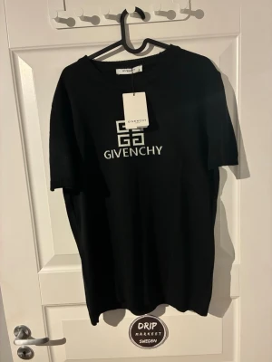 Svart Givenchy t-shirt med logga - Snygg svart t-shirt från Givenchy med vit logga och grafiskt tryck på bröstet. Klassisk rund hals och korta ärmar. Perfekt för dig som vill ha en stilren och exklusiv look med streetwear-vibe.