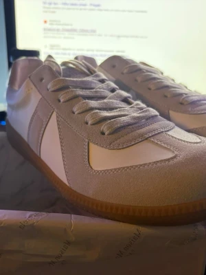 Vita och beige sneakers med mockadetaljer - Snygga sneakers i vitt och beige med ovandel i slätt läder och mockadetaljer. Klassisk siluett med gummisula i brunt och matchande vita skosnören. Perfekta för en clean och stilren look.