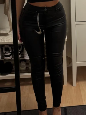 Svarta slim byxor med hög midja - Snygga svarta byxor med hög midja och slim passform. Byxorna har klassisk femficksdesign, bälteshällor och stängs med knapp och dragkedja. Perfekta för dig som gillar en stilren och enkel look.