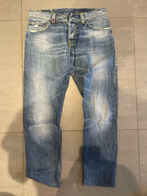 Dondup - Säljer ett par blå jeans med rak passform och slitna detaljer. Jeansen har klassisk femficksdesign, ljusa tvättade partier och slitningar på både fram- och baksida. Materialet är denim i bomull och de har kontrastsömmar för en cool look.