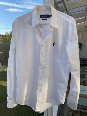 Polo Ralph Lauren vit Custom Fit skjorta - Klassisk vit Polo Ralph Lauren-skjorta i Custom Fit, storlek S / 165/88A men passar som XS.  Stilren vit modell med mörkblå broderad Pony-logga på bröstet. Sparsamt använd och i mycket bra skick utan större slitage.  Motsvarande Custom Fit Oxford-skjorta kostar cirka 1 895 kr ny hos Ralph Lauren idag. Säljes pga fel storlek.