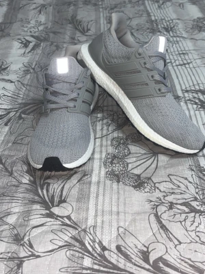 Gråa sneakers ultra boost med vit sula - Snygga grå sneakers med stickad ovandel och vit, dämpad sula. Skorna har gråa snören och detaljer i plast längs sidorna. Perfekta för dig som gillar en clean och sportig look. Passar till det mesta och är riktigt bekväma.