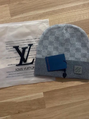 Fin mössa - Snygg grå mössa från Iv med klassiskt rutmönster och diskret logotyp framtill. Tillverkad i mjuk ullmix som håller dig varm och stilren. Perfekt accessoar för dig som vill ha en exklusiv touch på din outfit.