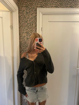 Mörkgrå oversized kofta - Mysig mörkgrå kofta med oversized passform och v-ringad hals. Koftan har knäppning framtill med flera knappar och långa ärmar. Perfekt att slänga över ett linne eller t-shirt för en avslappnad look.