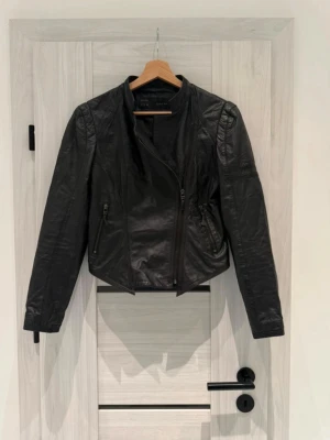 Zara Basic Real Leather Jacket - 100% Lambs Leather - Säljer en fantastiskt snygg och tidlös skinnjacka från Zara Basic. Tillverkad i mjukt, högkvalitativt 100% lammläder (Piel de Cordero). Jackan har en figursydd passform med snygga dragkedjedetaljer och en modern krage – en klassiker som håller i många år!  Märke: Zara Basic  Storlek: S (EUR S / USA S / MEX 26)  Material: 100% äkta lammläder (Foder: 100% polyester)  Färg: Svart  Skick: väl omhändertagen och naturligt mjukt läder (inga skador) 🚫 Hem: Rök- och djurfritt hem 🚚 Fraktar inom 24h!