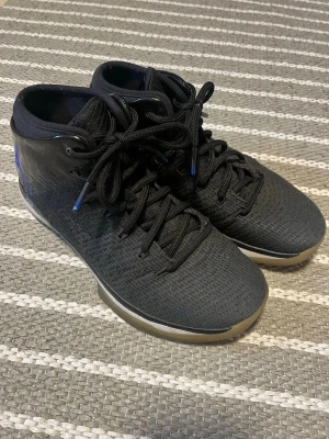 Svarta Jordan sneakers  - Svarta Jordan sneakers med blå Jumpman-logga på hälen. Skorna har högt skaft, svarta skosnören och ovandel i mesh och syntetmaterial. Sulan är vit med genomskinliga detaljer. 