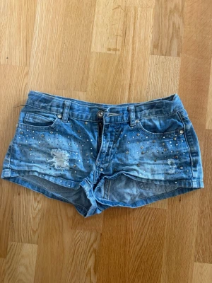 Blå jeansshorts med nitar - Säljer ett par blå jeansshorts med coola slitningar och silverfärgade nitar framtill. 