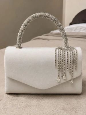 Vit kuvertväska med strasshandtag - Stilren vit kuvertväska med böjt handtag täckt av glittrande strass. Väskan har en mjuk, sammetsliknande yta och dekoreras framtill med hängande strassdetaljer och droppformade kristaller. Perfekt accessoar för att lyfta din outfit.