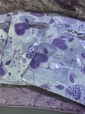 300st plast påsar med hjärtmönster - Säljer en söt påser i plast med lila hjärtan och blommor på vit bakgrund. Väskan har utskuret handtag och är perfekt för att bära mindre saker. Mönstret är lekfullt och färgerna ger en fräsch vibe. Antal 300st 