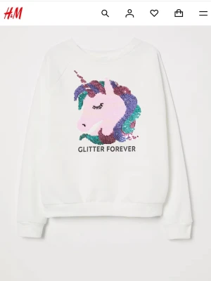 Vit tröja med paljett-unicorn - Vit sweatshirt från H&M med färgglatt enhörningsmotiv (unicorn) och paljetter som ändrar färg. Storlek 158/164 men den skulle också passa mig som har storlek S.  Aldrig använd och i nyskick. Har endast förvarats i garderoben. Tröjan har rund hals och ribbade muddar och midjan. Perfekt för dig som älskar färg och glitter.