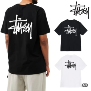 Svart Stüssy t-shirt med logga - Streetwear t-shirt från Stüssy i svart bomull med stor vit logga på ryggen och mindre logga på bröstet. Klassisk passform och korta ärmar, perfekt för en avslappnad och trendig look. Stüssy is designed with a relaxed, loose fit based on US sizing, so the overall width and length tend to run slightly roomy.  Please note that the fit may vary depending on your body type and personal preference.  We strongly recommend checking the detailed size chart below before making your purchase.