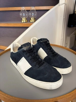 Valentino blåa och vita sneakers - Snygga sneakers från Valentino i mörkblå mocka med vita läderdetaljer. Skorna har en vit sula och coolt mönster undertill. Perfekta för dig som vill ha en stilren men ändå unik look. Väldigt fräscha och bra skick men det saknas 3 respektive 2 spikar på skorna. Pris kan disskuteras