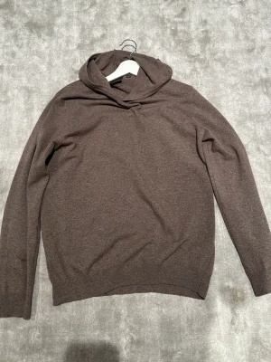 Brun stickad hoodie Oscar Jacobson - Säljer en brun stickad hoodie från Oscar Jacobson. Tröjan har en avslappnad passform, lång ärm och ribbade muddar. Tillverkad i Italien och känns riktigt mjuk och skön. Perfekt för dig som gillar stilrena och klassiska plagg.