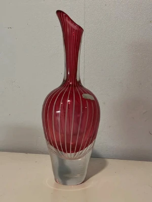 Röd glasvas med vita ränder - Unik glasvas i rött med vita vertikala ränder och transparent fot. Vasen har en elegant, smal hals och rundad kropp som ger ett modernt intryck. Perfekt som dekoration i hemmet eller för snittblommor.