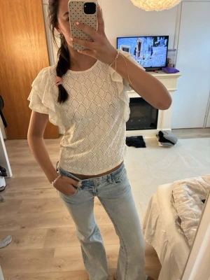 Vit blus med volangärmar - Söt vit blus med volangdetaljer på ärmarna och ett diskret rutmönster. Blusen har rund halsringning och är tillverkad i ett lätt, luftigt material som passar perfekt till jeans eller kjol. Perfekt för dig som gillar en romantisk och fräsch stil.
