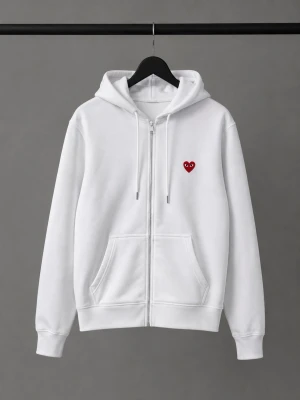 Vit hoodie med rött hjärta - Säljer en clean vit hoodie med dragkedja och huva. På bröstet finns ett broderat rött hjärta med ögon, vilket ger en unik och trendig look. Hoodien har kängurufickor och ribbade muddar. Perfekt för dig som gillar stilrena plagg med en twist.