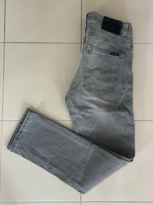 Nudie Jeans - Gråa Nudie Jeans i toppskick! Jeansen är i väldigt skönt material och har en mycket behaglig passform. Riktigt fräsch och snygg badge dessutom! Längd - 99 cm och Bredd - 39 cm. 