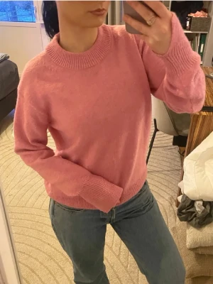 Rosa stickad tröja med rund hals - Mysig rosa stickad tröja med rund halsringning och ribbade muddar vid ärmslut och nederkant. Tröjan har en avslappnad passform och är perfekt för att hålla värmen under kyliga dagar. Passar till både jeans och kjol för en enkel, snygg look.