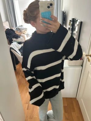 Svartvit randig oversized stickad tröja - Säljer en oversized stickad tröja med breda svarta och vita ränder. Tröjan har hög krage och långa ärmar med nedhasad axelsöm. Perfekt för dig som gillar en avslappnad och trendig look.