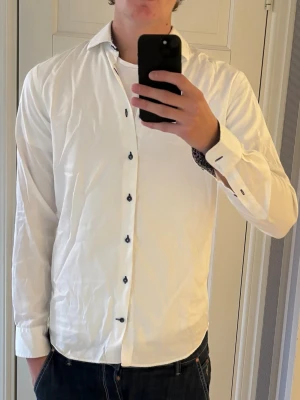 John Henric Skjorta - Ursnygg skjorta från John Henric i storlek 39! Skjortan är väldigt skön och i bra skick och har ett riktigt snyggt mönster i halsen och ärmarna! En liten defekt är att knappen längst ner har lossnat.