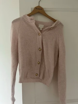 Ljusrosa kofta från H&M - Mysig ljusrosa kofta från H&M med ribbstickad struktur och guldfärgade knappar framtill. Koftan har rund halsringning, långa ärmar och en mjuk, fluffig känsla. Perfekt att slänga över en topp för extra värme.