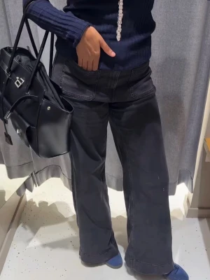 Svarta vida jeans med stora fickor - Säljer ett par svarta jeans med bred passform och stora framfickor. Jeansen har hög midja och raka, vida ben som ger en avslappnad och trendig look. Perfekta för dig som gillar streetstyle och vill ha något bekvämt men snyggt.