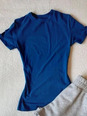 Blå tight t-shirt med rund hals - En enkel och stilren blå t-shirt med rund hals och tight passform. T-shirten har korta ärmar och är gjord i mjuk bomull som känns skön mot huden. Perfekt att matcha med jeans eller shorts för en clean look.