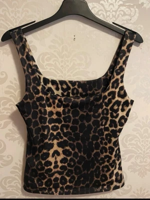 Leopardmönstrad ärmlös topp - Säljer en snygg leopardmönstrad topp med breda axelband och fyrkantig ringning. Toppen är figurnära och har en cool, djurinspirerad look som sticker ut. Perfekt för dig som vill ha något trendigt och vågat i garderoben.