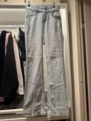 Ljusblå bootcut jeans - Säljer ett par ljusblå bootcut jeans med klassisk femficksdesign och låg midja. Jeansen har råa, fransiga benslut och är tillverkade i denim med en lätt tvättad look. Perfekta för en avslappnad och trendig stil. Midjemått 34 cm, från midja till skrevet 21 cm, innrebenslängd 82cm 