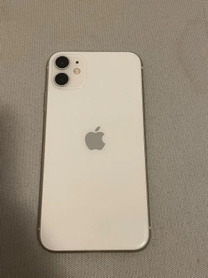 Vit iPhone 11 med dubbla kameror - Säljer en stilren vit iPhone 11 med två bakre kameror och snygg glasbaksida. Telefonen har rundade kanter och klassisk Apple-logga på baksidan. Perfekt för dig som gillar modern design och vill ha en pålitlig smartphone. 100% i batterikapacitet, batteriet är nytt så det står att mobilen inte kan läsa av batteriet ifall det är äkta eller fake. Den är väl använd, fungera alldeles utmärkt under min ägo, den är väldigt bra för att vara en iPhone 11. Skickas i en swappie kartong, då jag ej ha kartong