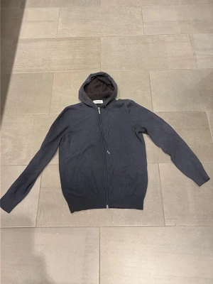 Mörkblå hoodie från Gran Sasso - Snygg mörkblå hoodie från Gran Sasso med dragkedja framtill och justerbar huva. Tillverkad i mjukt stickat material som känns lyxigt och bekvämt. Perfekt för dig som gillar en clean och stilren look. Passar till det mesta och är enkel att matcha. Nypris 3000. Vid frågor är det bara att höra av sig! Mvh Lion.
