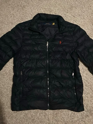 Marinblå pufferjacka från Polo Ralph Lauren - Säljer en marinblå jacka från Polo Ralph Lauren. Storleken är M och nypris ligger på 4000kr. Vid minsta fundering hör av dig! Priset är ej hugget i sten!