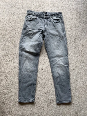 Jack n jones Jeans  - Säljer ett par grå jeans med rak passform och klassisk design. Jeansen har normal midja och knappgylf. Perfekta för en avslappnad och stilren outfit. Säljer jeansen då dom ej kommer till användning längre.