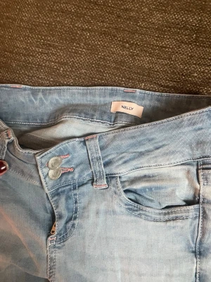 Ljusblå stitch jeans från Nelly med rosa detaljer - Säljer ett par ljusblå jeans från Nelly med dubbla knappar framtill och rosa sömmar. Baktill har fickorna en cool zigzag-detalj i rosa. Jeansen har klassisk femficksmodell och är i mjukt denimtyg. Perfekta för en avslappnad och trendig look. De är lite klippta nertill.