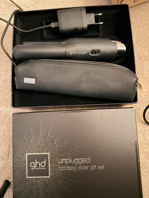 ghd Unplugged Cordless Styler Set - Snyggt presentset med ghd unplugged sladdlös plattång, svart värmetålig väska och laddare. Perfekt för styling on-the-go. Plattången är svart med silverdetaljer och har en smidig, kompakt design som passar i väskan.