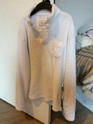 Vit fluffig stickad tröja Tallie - Supermjuk och fluffig vit stickad tröja från Tallie. Tröjan har en hög krage, liten bröstficka och långa ärmar. Perfekt för dig som gillar mysiga och stilrena plagg. Materialet känns riktigt gosigt och passar till många olika looks. Perfekt nu till kallare tider Storleken är M men sitter bäst som S