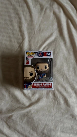 Funko Pop Sergio Ramos PSG #51 - Cool Funko Pop-figur av Sergio Ramos i PSG-tröja, nummer 51. Figuren är gjord av vinyl och kommer i originalförpackning med PSG-logga och tydlig design. Perfekt för samlare eller fotbollsfans som gillar unika prylar.
