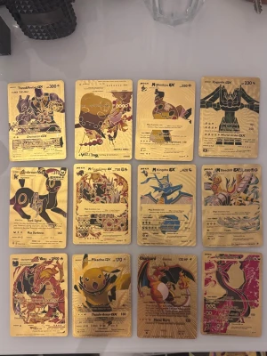 Pokémon samlarkort i guld - Säljer ett set med tolv exklusiva Pokémon samlarkort i guldfärgad metall. Korten har motiv av olika Pokémon som Pikachu, Charizard och Mewtwo, med detaljerade illustrationer och text. Perfekt för dig som vill ha något unikt till din samling eller som dekoration.