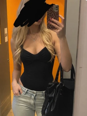Svart body med sweetheart-ringning - Snygg svart body med sweetheart-ringning och lätt rynkad detalj vid bysten. Bodyn har smala axelband och knäppning i grenen. Passar perfekt till jeans eller kjol för en stilren look. Materialet ser stretchigt och bekvämt ut.