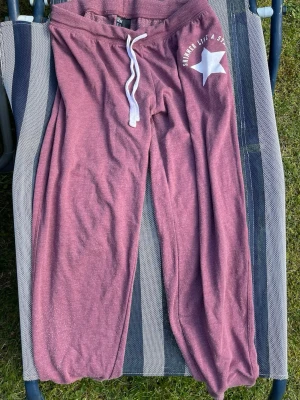 Purple Sweatpants with White Drawstring and Star Print - These are a pair of purple sweatpants featuring a white drawstring and a white star graphic on the left hip. The text around the star reads 'SHIN* LIKE A STAR'. The pants have a relaxed fit and cuffed ankles. The back is plain with no additional designs or pockets.