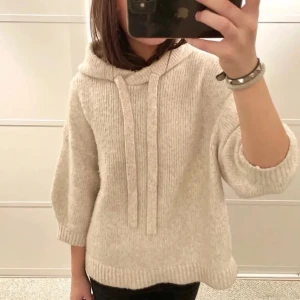 Beige trekvartsärmad hoodie med luva - Mysig beige stickad hoodie med luva och breda snören. Tröjan har trekvartsärmar och avslappnad passform. Perfekt för lager på lager och chill dagar. Stickad i mjukt material som känns skönt mot huden.💓 storlek xs passar också s